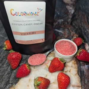 A bag of Colorwayz Strawberry Cotton Candy Sugar surrounded by fresh strawberries and a spoonful of pink sugar, showcasing natural ingredients and vibrant color.