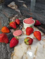 A small bowl filled with pink strawberry cotton candy sugar, surrounded by fresh strawberries on a marble surface, highlighting the natural ingredients and vibrant color.