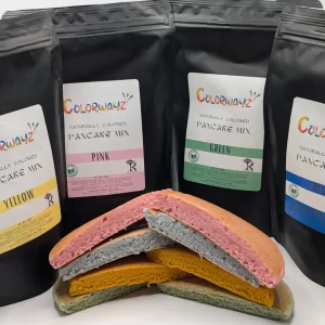 4 different colors of pancake mix with pancakes made in front of the bag. pink, blue, green, and yellow