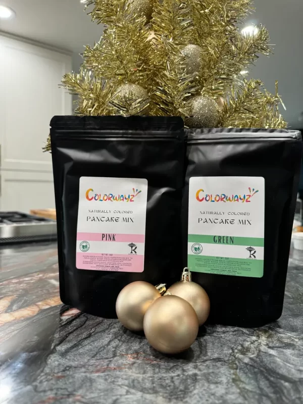 Colorwayz pink and green pancake mixes arranged with golden Christmas decorations, perfect for festive breakfasts.